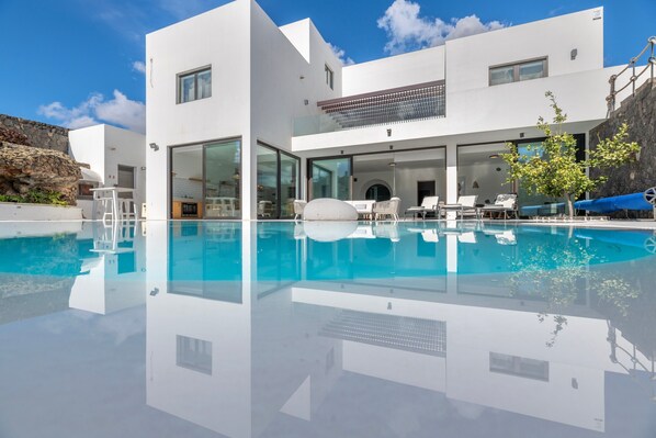 Une maison moderne dotée d’une piscine, d’un espace salon extérieur et d’un mur en pierre.