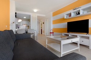 En moderne stue med sofa, sofabord, tv og et køkken i baggrunden.