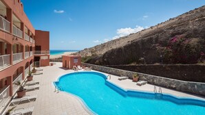 A swimming pool with lounge chairs, a small poolside area, and a view of the beach. - Vacation 'Home Sweet Home with Ocean View' with Sea View, Shared Pool and Wi-Fi (Costa Calma)