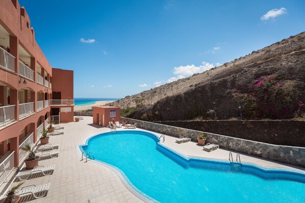 Ein Swimmingpool mit Liegestühlen, eine kleine Pool-Terrasse und Blick auf den Strand.