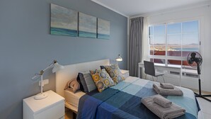 A bedroom with a bed, a nightstand, a desk, a chair, a window with a view, and a fan. - Vacation 'Home Sweet Home with Ocean View' with Sea View, Shared Pool and Wi-Fi (Costa Calma)