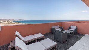 A balcony with outdoor furniture, a view of the sea, and a distant landscape. - Vacation 'Home Sweet Home with Ocean View' with Sea View, Shared Pool and Wi-Fi (Costa Calma)