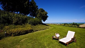 Une pelouse verdoyante avec un fauteuil de jardin et une petite table, le tout entouré d’une végétation luxuriante et offrant une vue dégagée sur l’océan.