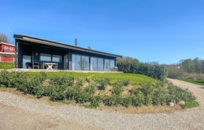 Une maison moderne dotée de grandes fenêtres en verre, d’un patio couvert et d’une allée en gravier.
