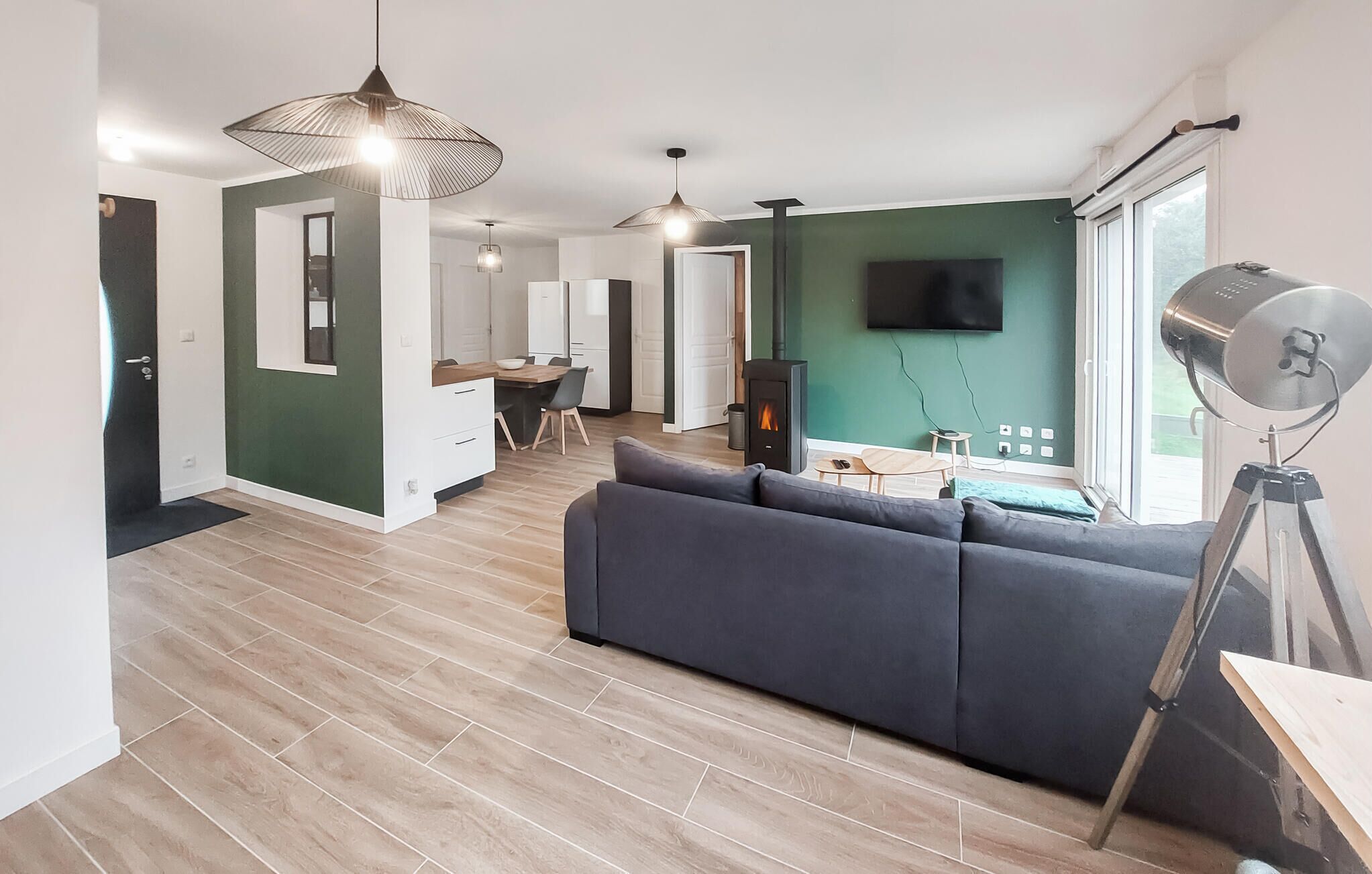 A modern living room with a sofa, a dining area with a table and chairs, a TV mounted on the wall, and a fireplace.