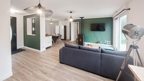 Una sala moderna con un sofá, un comedor con mesa y sillas, un televisor montado en la pared y una chimenea.