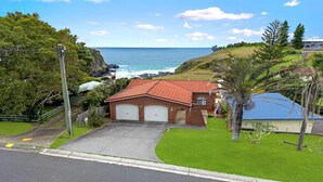 A coastal house with a red roof, two garage doors, and a well-maintained lawn.