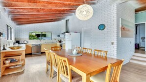 A modern kitchen with white brick walls, wooden ceiling beams, and a dining area with a wooden table and chairs.