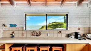 A kitchen with a large window overlooking a beach and hills. There are kitchen appliances, a coffee maker, and a sign that says "NO SMOKING".