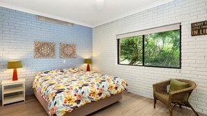 A bedroom with a bed, two wall-mounted lamps, a wicker chair, and a window with a view of trees.