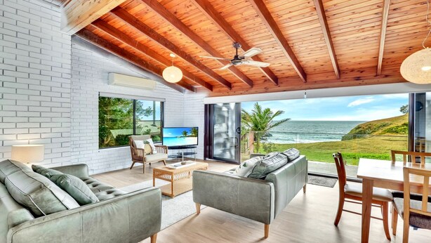 A modern living room with a large TV, comfortable seating, and a view of the ocean.