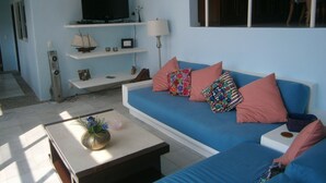 Een woonkamer met een blauwe bank, een bijzettafeltje met een vaas en een flatscreen televisie op een meubel.