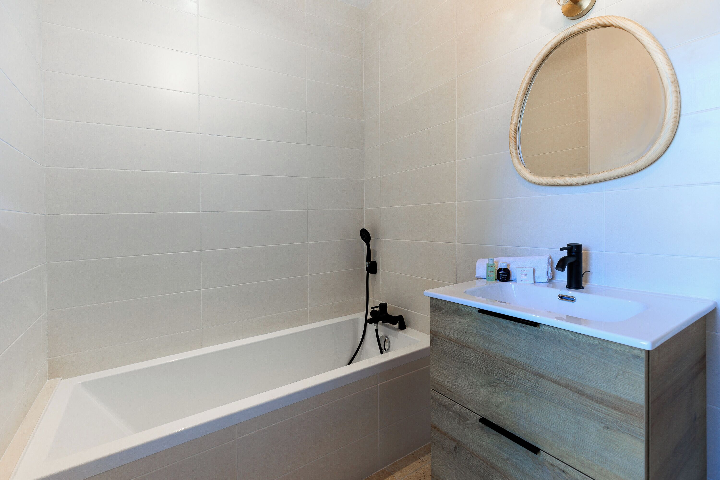 Een moderne badkamer met een wit bad, een houten wastafelmeubel met spiegel, en een witte wasbak.