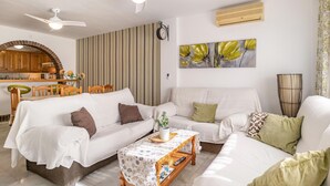 Una sala de estar con un sofá blanco, una mesa de centro y un comedor con sillas de madera y una cortina a rayas.