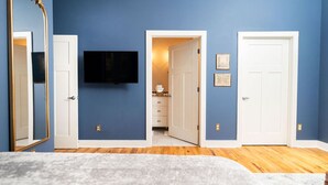 A bedroom with a bed, a TV mounted on the wall, and two doors leading to other rooms.
