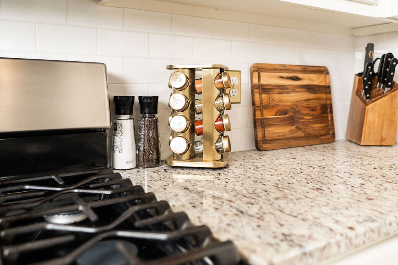 A kitchen with a gas stove, a spice rack, a wooden cutting board, and a knife block.