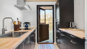 A modern kitchen with a stainless steel sink, a coffee machine, and a view through an open door. - 3 bedroom cozy home in Martofte (Martofte)
