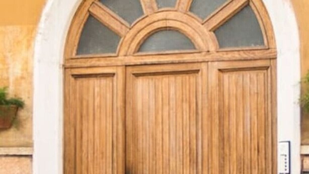Una puerta doble de madera con un arco semicircular encima, ubicada en una pared de piedra.