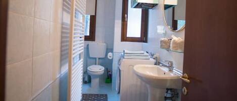 A narrow bathroom with a toilet, sink, and a small window.