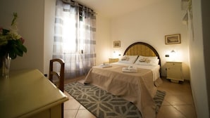 Un dormitorio con cama, mesitas de noche, una silla, escritorio y ventana con cortinas.