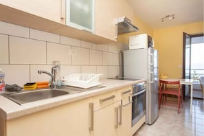 A modern kitchen with a sink, stove, and refrigerator, a dining area with a table and chairs, and a window providing natural light. - Holiday apartment with fantastic sea views (Ravni)
