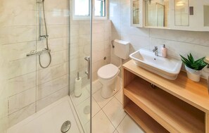 Une salle de bain moderne avec une douche à parois de verre, des toilettes, un lavabo avec un miroir au-dessus et une plante en pot.