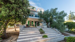 Un bâtiment à deux étages, doté d’un escalier en pierre menant à un espace extérieur aménagé, abrité par un toit.
