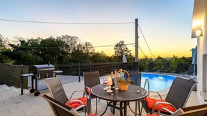 Un patio al aire libre con piscina, sillas, una mesa y una parrilla.