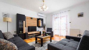 Una sala de estar moderna con un televisor de pantalla plana, un mueble de madera y dos sofás grises.