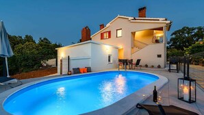 Una casa moderna de dos pisos con piscina, zona de estar al aire libre y una escalera que lleva a un nivel superior.