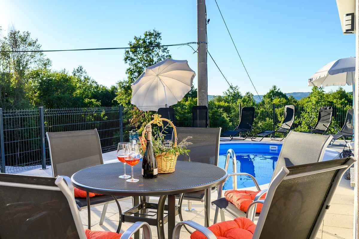 Un espace aménagé au bord de la piscine, avec une table dressée pour deux personnes, une bouteille de champagne et un panier de fleurs.