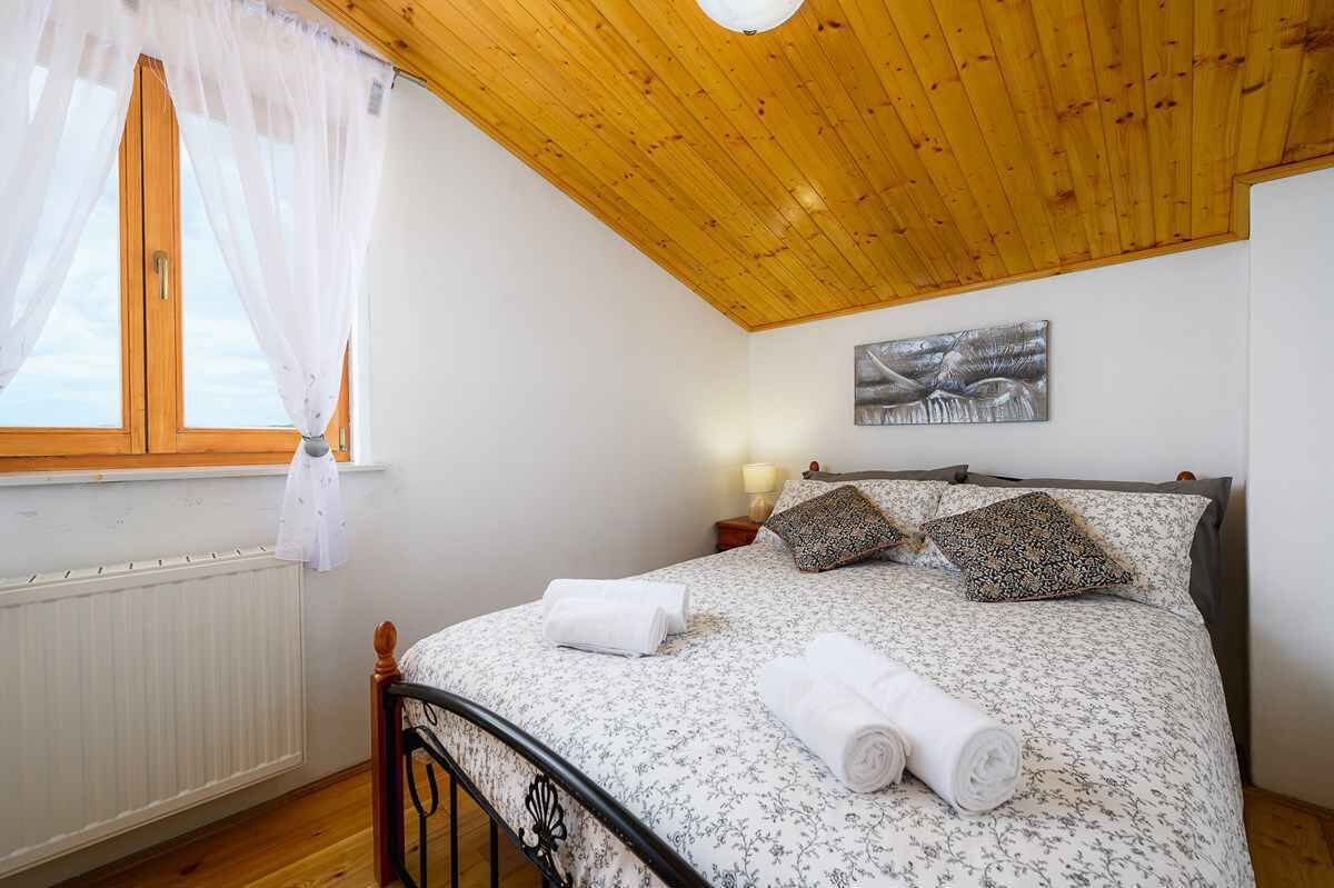A bedroom with a wooden ceiling, a bed with floral bedding, two pillows, and a rolled towel on the bed.