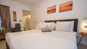 Una habitación de hotel con una cama grande, dos cuadros colgados en la pared, una mesita de noche con lámpara y una puerta de madera.