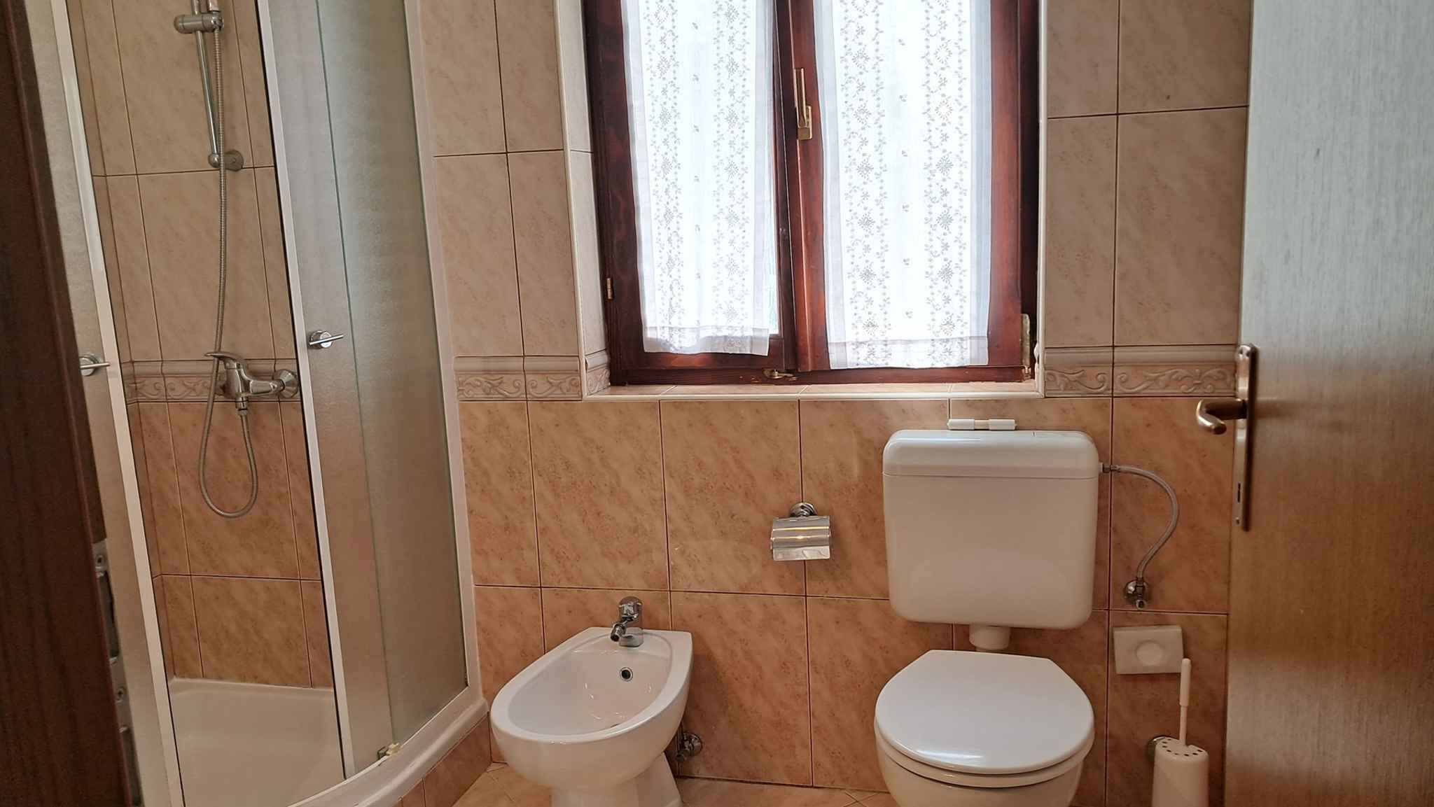 Ein Badezimmer mit Dusche, Bidet, Toilette und einem Fenster mit Vorhängen.