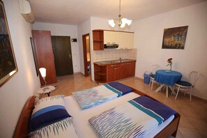 Een kamer met twee bedden, een kleine kitchenette, een eettafel met stoelen en een schilderij aan de muur.