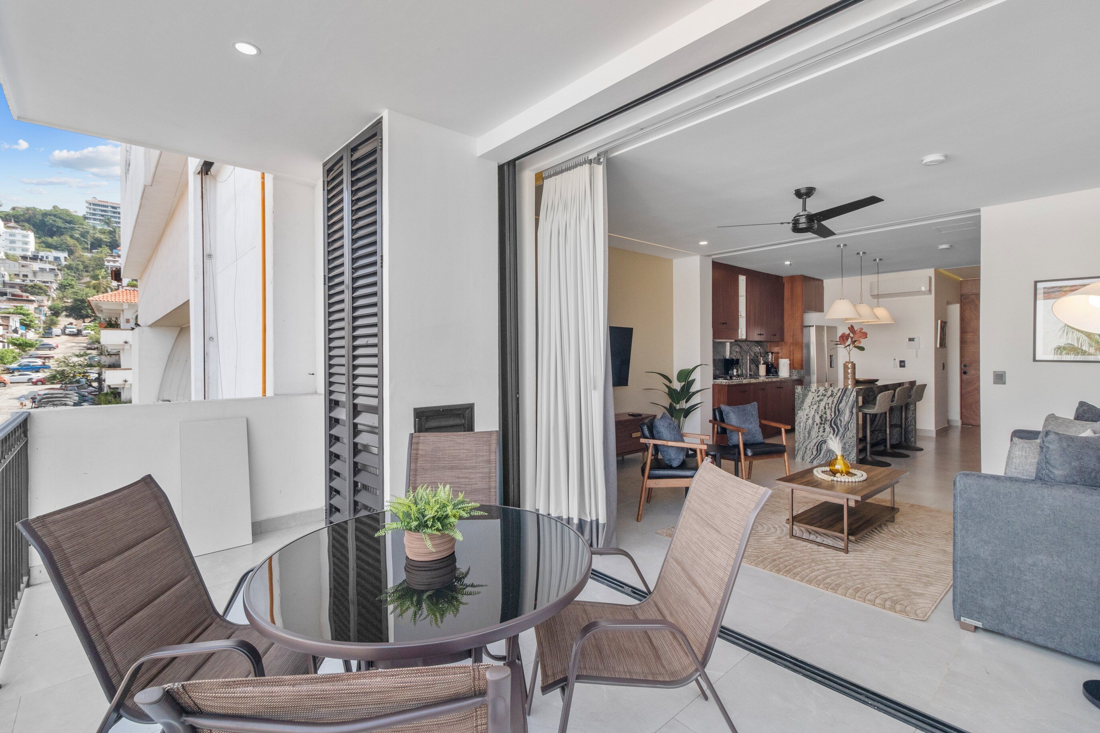 A modern apartment with a balcony, a dining area with a glass table, and a living room with a sofa and a coffee table.