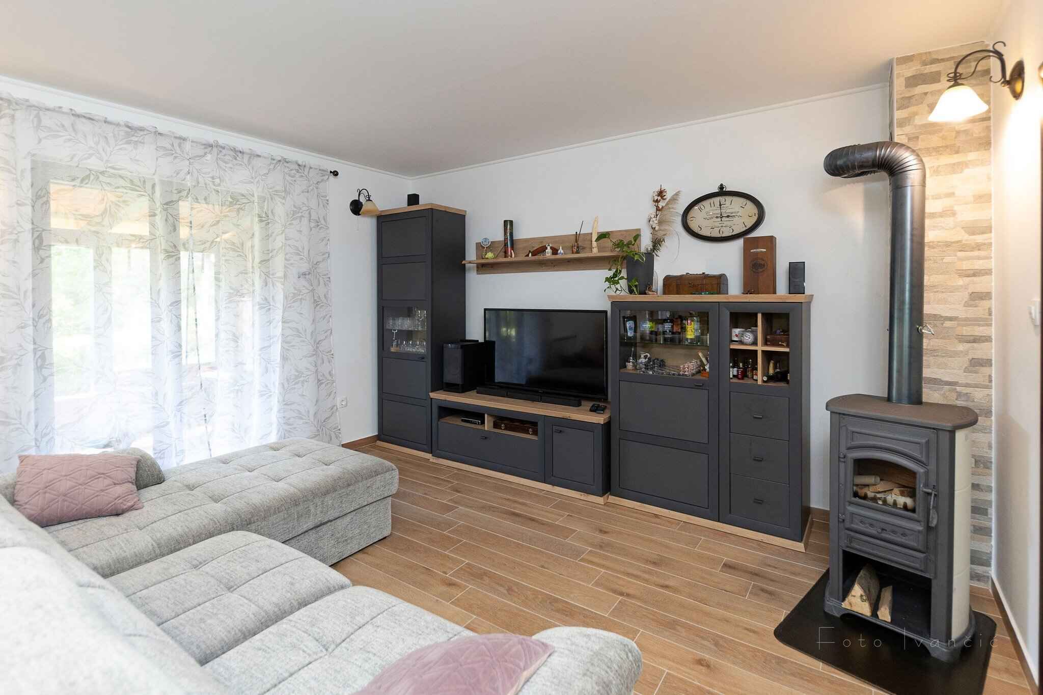 Una sala de estar moderna con un sofá gris, un televisor de pantalla plana, estanterías empotradas, una chimenea y un reloj en la pared.
