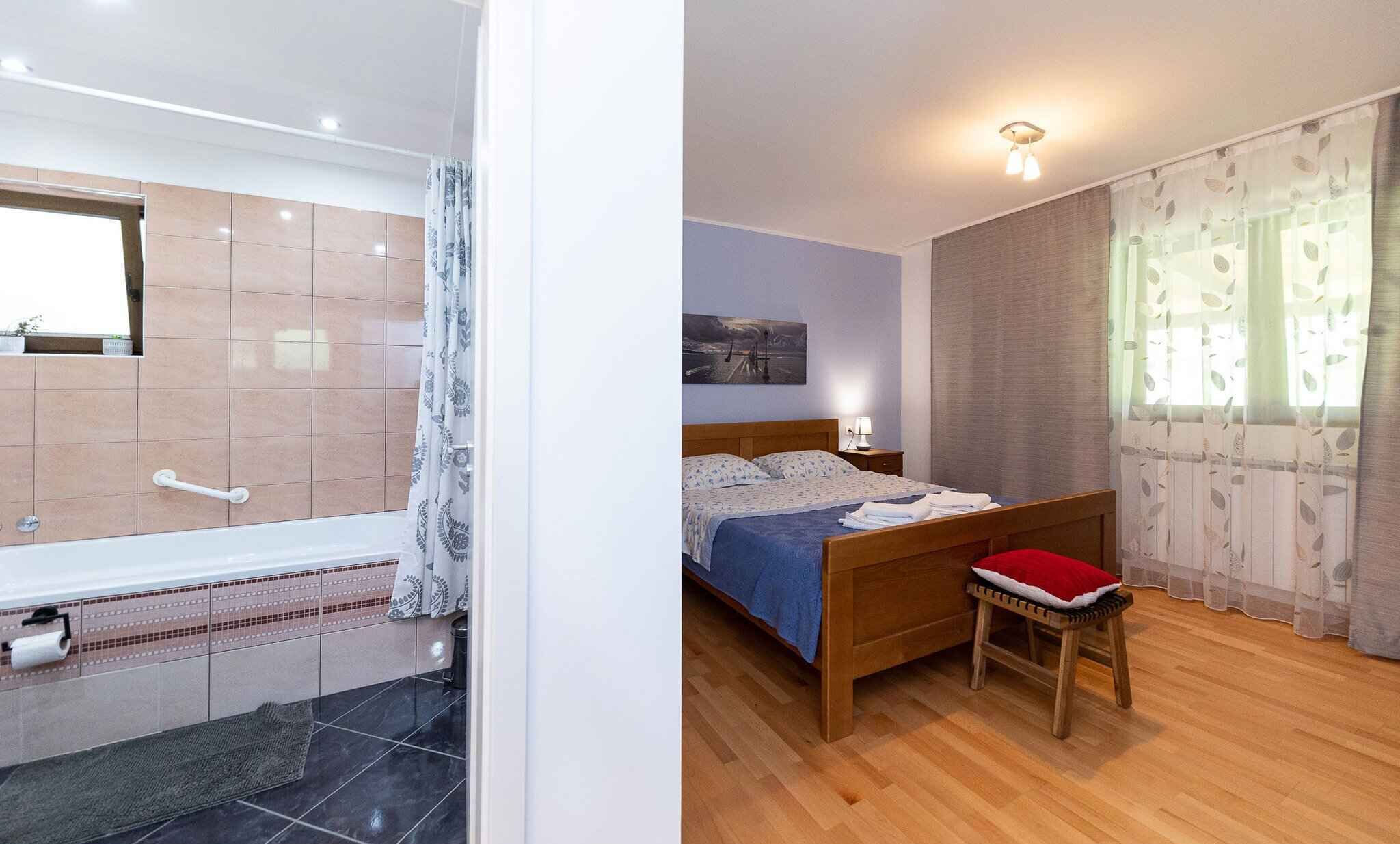 A bathroom with a bathtub, a toilet, and a shower area. The bedroom has a bed, a nightstand, and a window with curtains.