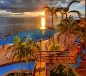 A resort pool area with a sunset view, wooden deck, and palm trees. - Tropical Executive Suit 1006 (Manaus)