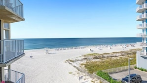 A beach view from a balcony with a clear sky, sandy beach, and a parking area.