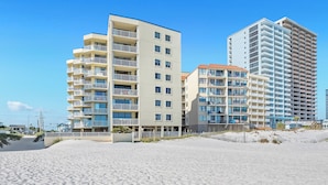 A beachfront hotel with multiple floors, balconies, and a sandy beach in the foreground.