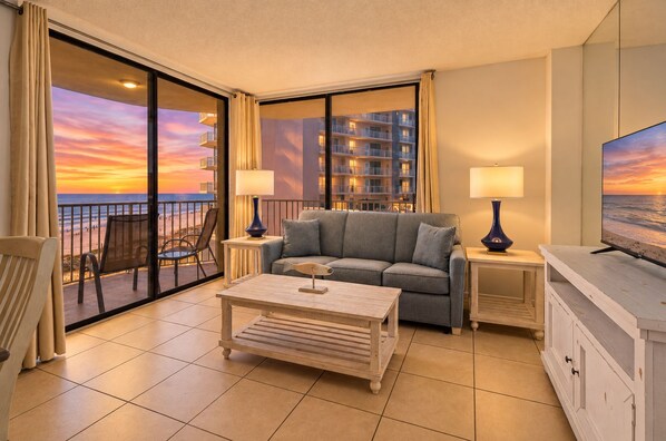 A hotel room with a balcony, a sofa, a coffee table, and a TV.