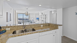 A kitchen with granite countertops, stainless steel sink, white cabinets, and a dishwasher.
