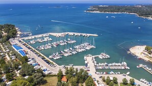 An aerial view of a marina with numerous boats docked, surrounded by greenery and a clear blue sea. - Holiday apartment in a beautiful setting, with air conditioning (Funtana)