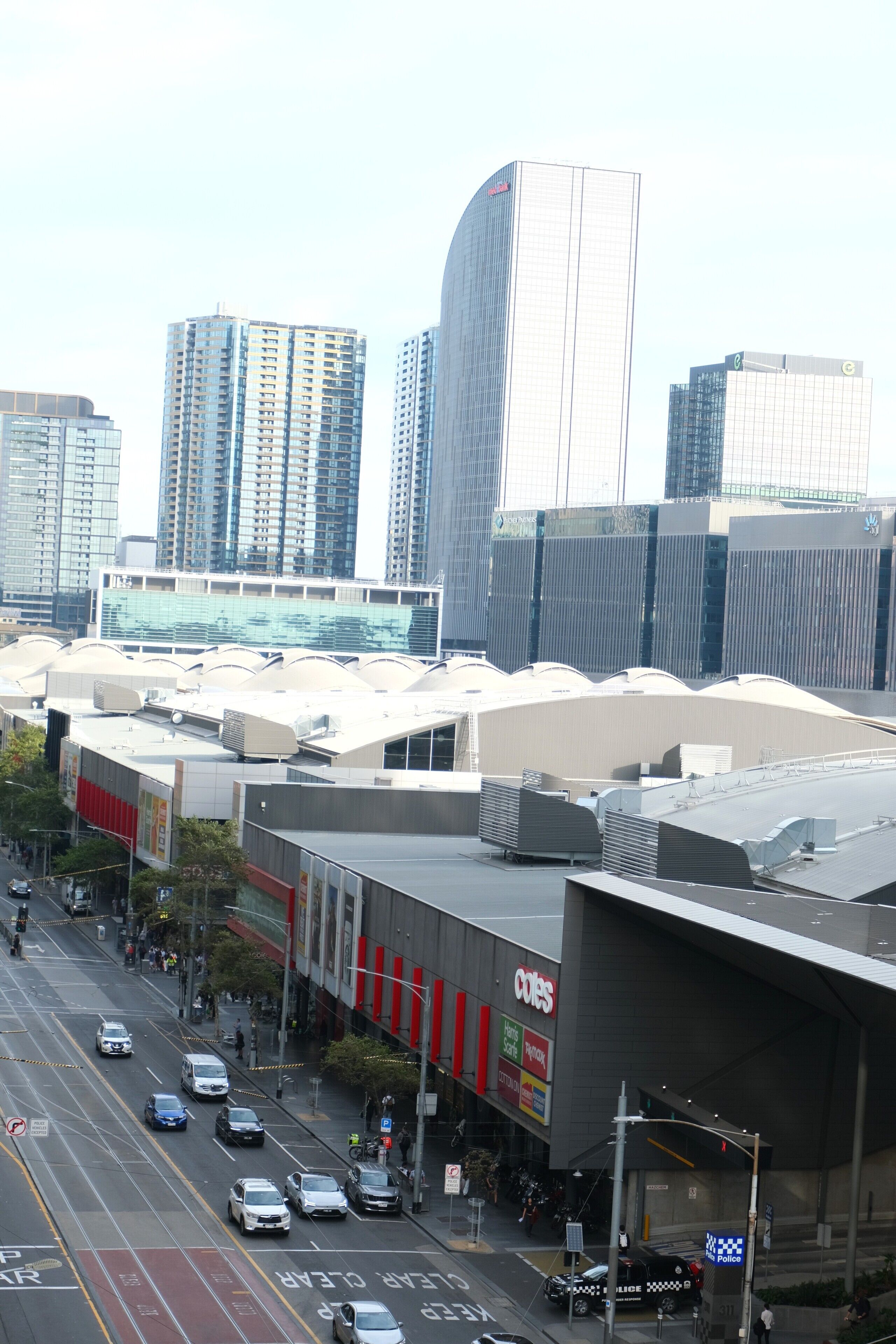 A cityscape with high-rise buildings, a street with cars, and a large commercial building with a sign.