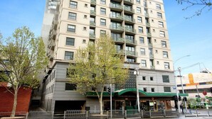 Un immeuble à plusieurs étages, doté d’une façade beige, de nombreux balcons et d’une entrée au niveau du sol surmontée d’un auvent vert.
