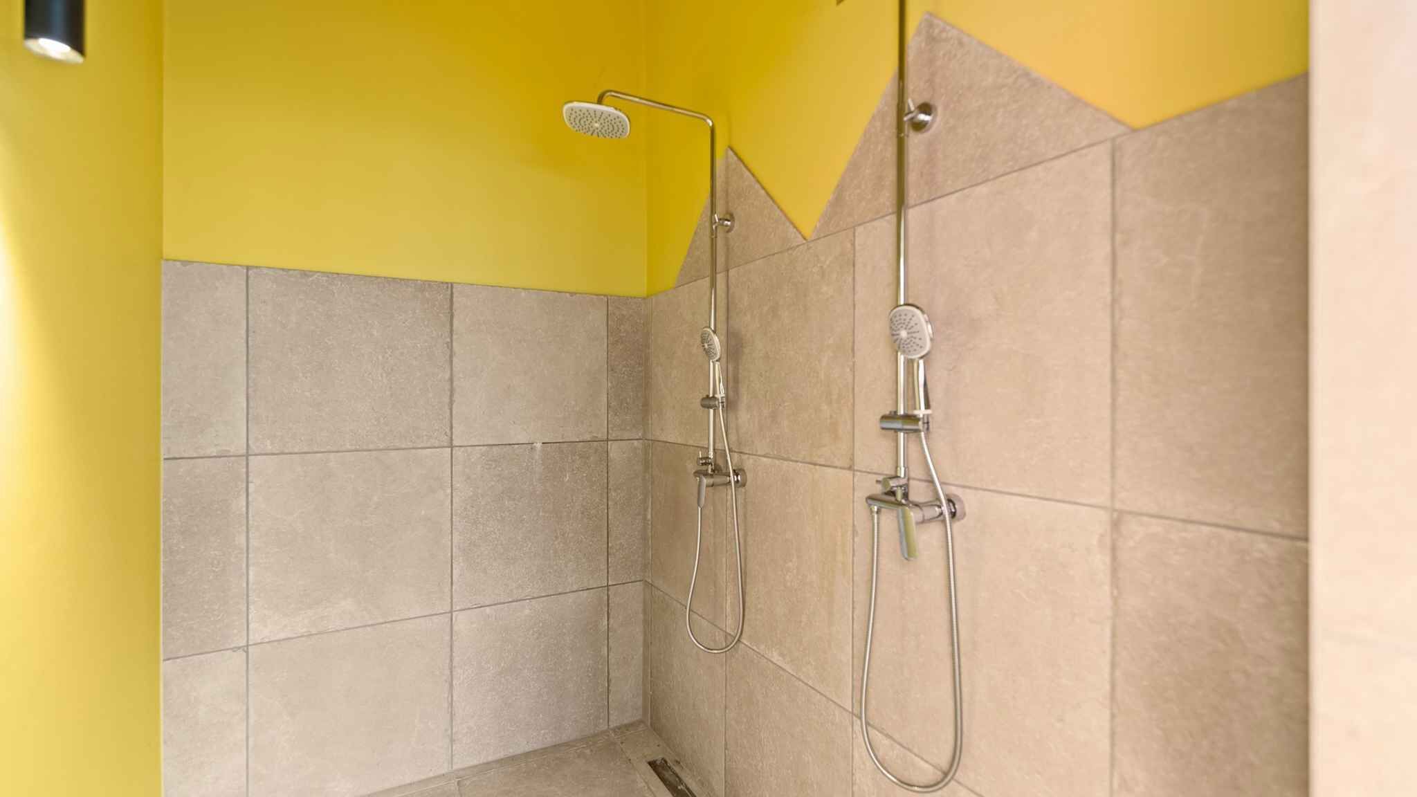 Eine Dusche mit Handbrause und fest installierter Duschbrause, geflieste Wände und einer gelben Akzentwand.