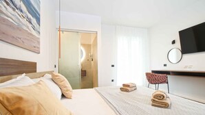 Hotellihuone, jossa on sänky, työpöytä, tuoli, televisio ja taulu seinällä.
