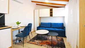 A compact living space with a kitchenette, a blue sofa, a dining table with two chairs, and a small rug. - Holiday apartment with air conditioning (Pula)