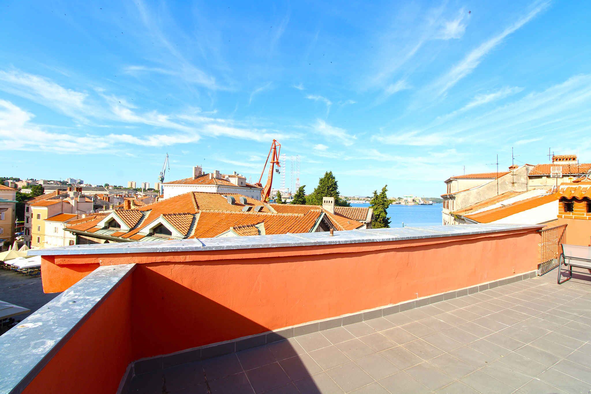 Une terrasse sur le toit aux murs orange, avec vue sur la ville et une grue visible au loin.